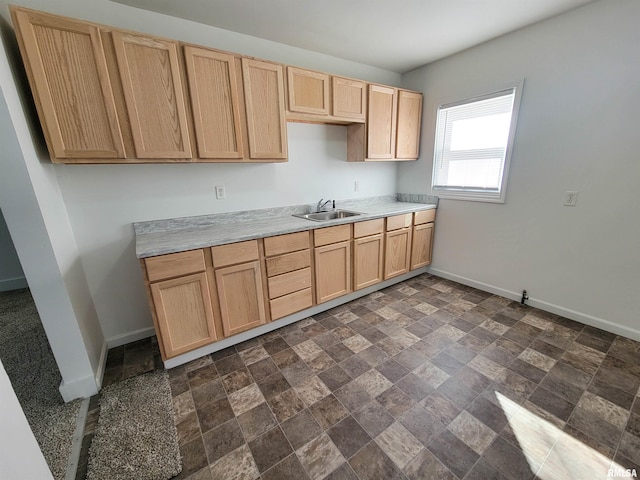 kitchen with light countertops, light brown cabinets, a sink, and baseboards