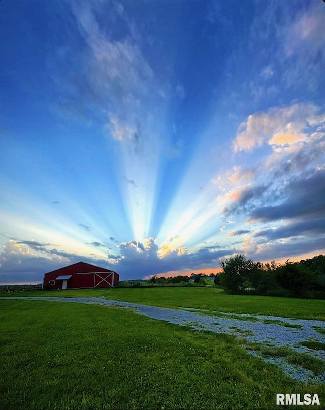 yard at dusk with a detached garage, a rural view, and an outbuilding