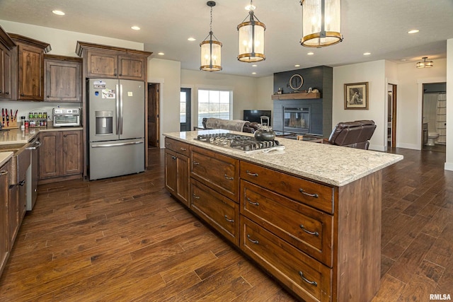 kitchen featuring open floor plan, stainless steel appliances, dark wood-type flooring, and a brick fireplace