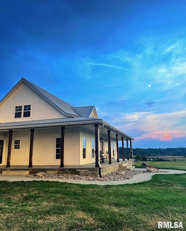 property exterior at dusk featuring a yard, covered porch, and metal roof