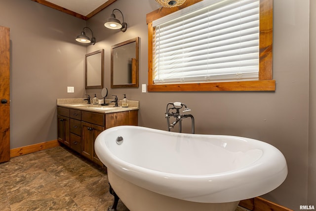 full bath featuring double vanity, a freestanding bath, baseboards, and a sink