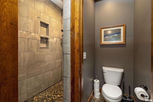 full bath featuring toilet, baseboards, and tiled shower