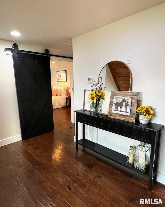 hallway with a barn door, wood finished floors, and baseboards