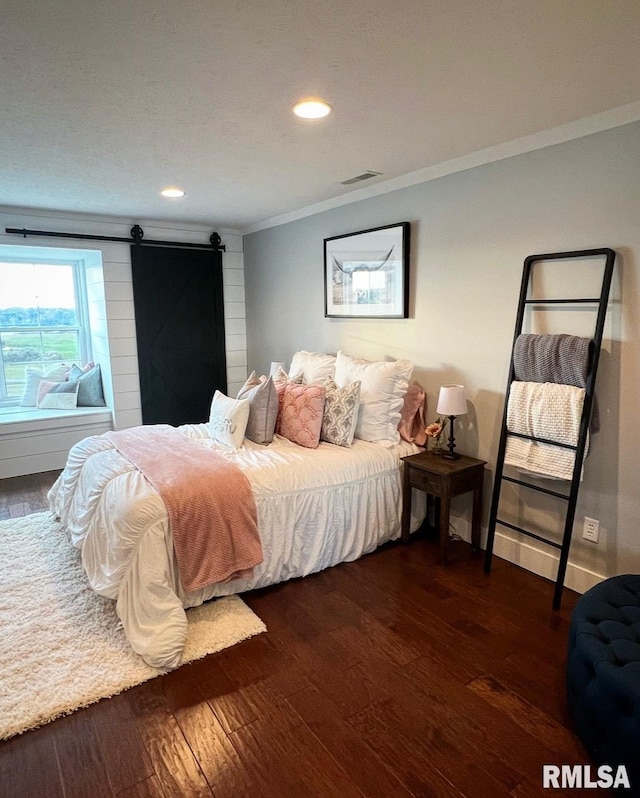 bedroom with a barn door, visible vents, baseboards, dark wood-style floors, and crown molding