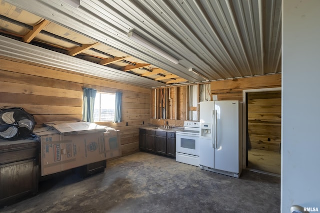 kitchen featuring unfinished concrete flooring, white appliances, a sink, and wood walls