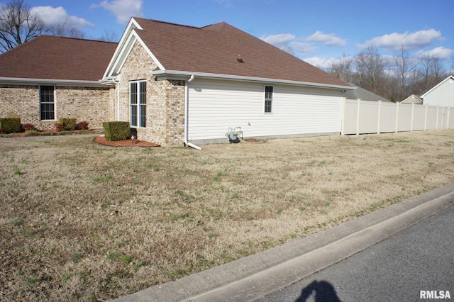 view of property exterior with a yard, brick siding, roof with shingles, and fence