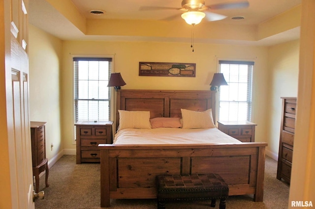 carpeted bedroom with a ceiling fan, a raised ceiling, visible vents, and baseboards