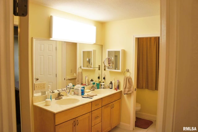 full bathroom with baseboards, a sink, toilet, and double vanity