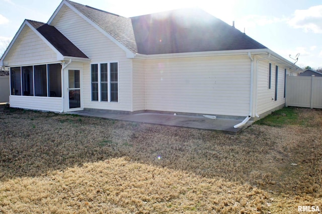 rear view of house featuring roof with shingles, a yard, a sunroom, a patio area, and fence