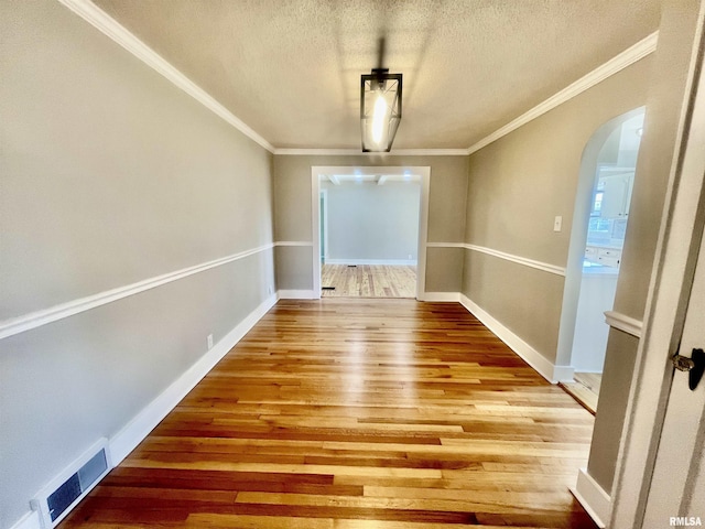 unfurnished dining area with arched walkways, crown molding, visible vents, a textured ceiling, and wood finished floors