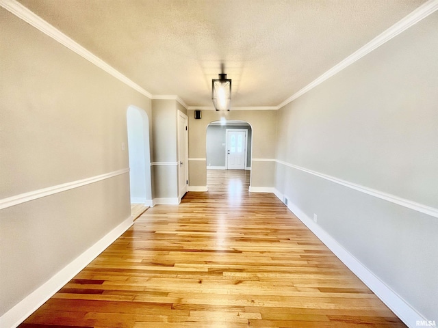 unfurnished dining area with light wood-style flooring, arched walkways, a textured ceiling, and ornamental molding