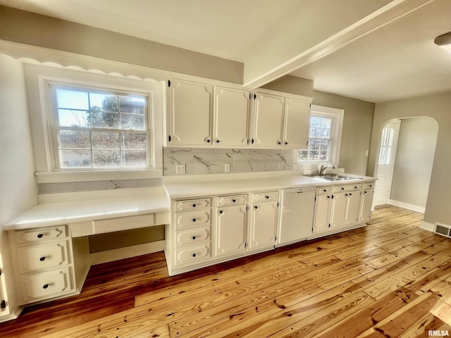 kitchen featuring arched walkways, decorative backsplash, light wood-type flooring, white cabinetry, and a sink