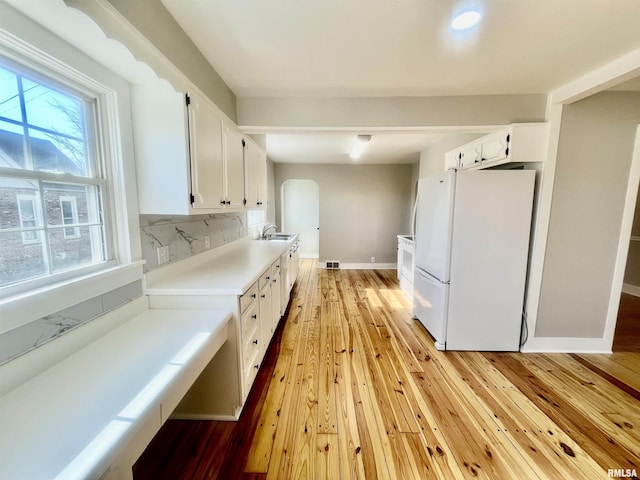 kitchen featuring light wood-type flooring, freestanding refrigerator, white cabinetry, and a sink