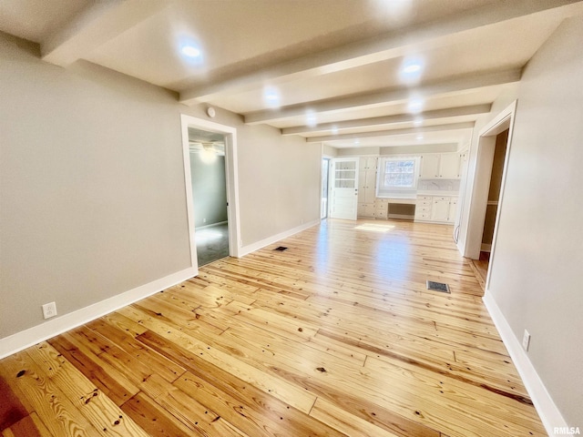 empty room featuring light wood-type flooring, visible vents, beamed ceiling, and baseboards