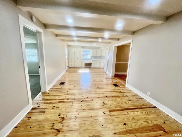 hallway featuring baseboards, beamed ceiling, and light wood-style floors