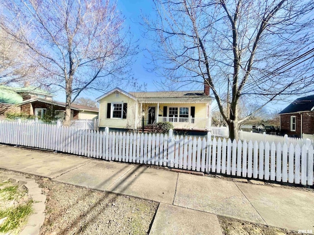 bungalow with covered porch, a fenced front yard, and a chimney