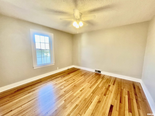 unfurnished room featuring baseboards, visible vents, a ceiling fan, wood finished floors, and a textured ceiling