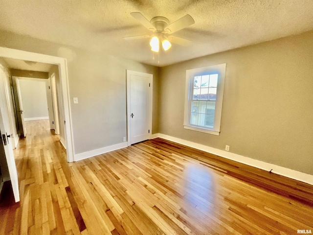 unfurnished bedroom featuring a ceiling fan, light wood-style flooring, baseboards, and a textured ceiling