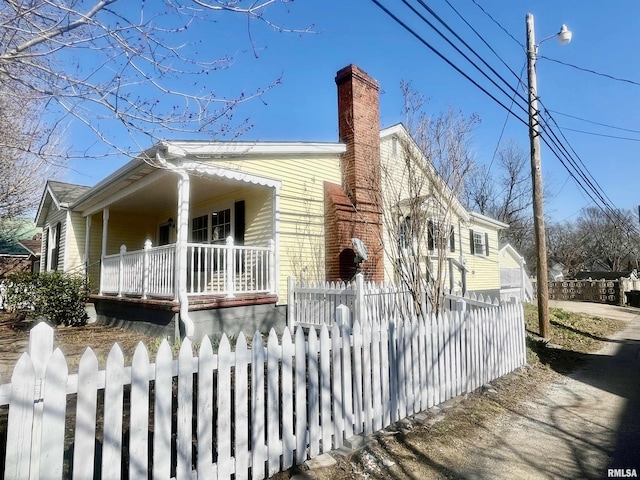 view of property exterior featuring covered porch, a fenced front yard, and a chimney