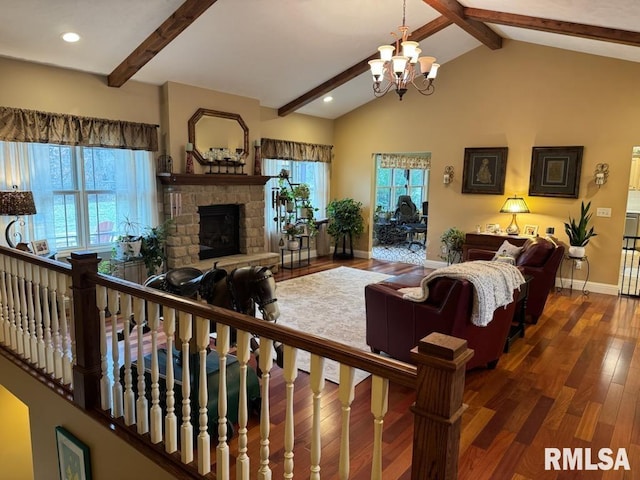 living room featuring baseboards, lofted ceiling with beams, a stone fireplace, an inviting chandelier, and wood finished floors