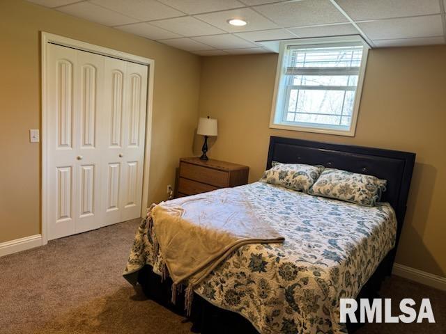 carpeted bedroom with a closet, a paneled ceiling, and baseboards