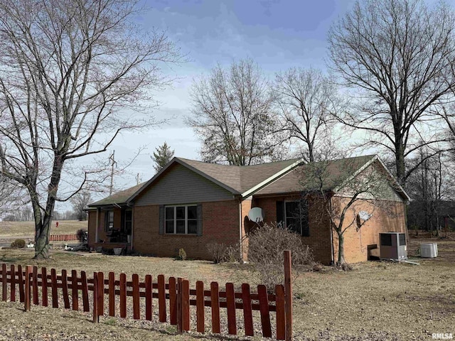 view of front of property with brick siding, a fenced front yard, and central AC unit