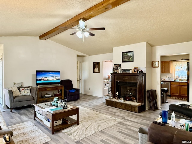 living area featuring light wood-type flooring, vaulted ceiling with beams, a fireplace with raised hearth, and a textured ceiling