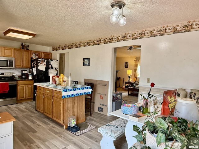 kitchen featuring light wood-style flooring, appliances with stainless steel finishes, a kitchen island, a textured ceiling, and ceiling fan