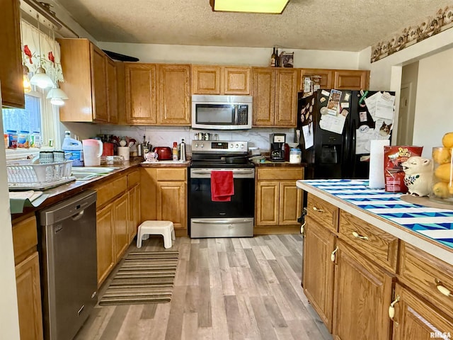 kitchen featuring tasteful backsplash, appliances with stainless steel finishes, brown cabinetry, a textured ceiling, and light wood-type flooring