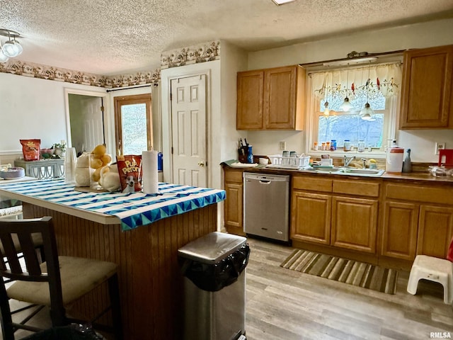 kitchen featuring brown cabinetry, dishwasher, light wood-style flooring, a breakfast bar, and a sink