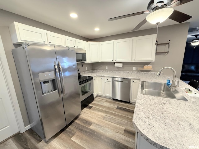 kitchen with a peninsula, light wood-type flooring, stainless steel appliances, and a sink