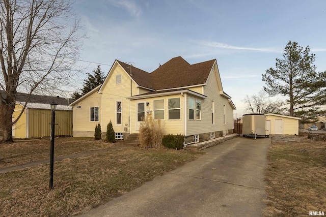 view of side of home featuring entry steps, a storage shed, a shingled roof, an outdoor structure, and concrete driveway