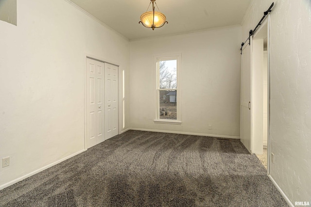 unfurnished bedroom featuring crown molding, a closet, a barn door, carpet flooring, and baseboards