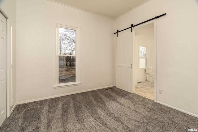 carpeted empty room featuring plenty of natural light, crown molding, baseboards, and a barn door