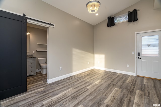 unfurnished dining area with wood finished floors, vaulted ceiling, baseboards, and a barn door