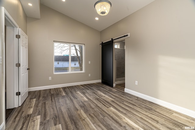 unfurnished bedroom with a barn door, recessed lighting, baseboards, vaulted ceiling, and dark wood finished floors