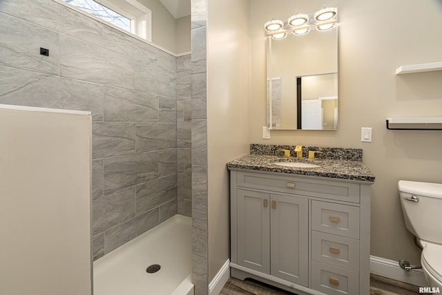 bathroom with baseboards, a tile shower, vanity, and toilet