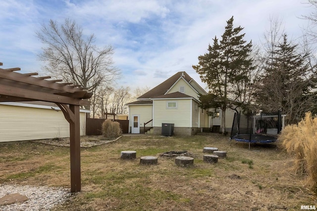 rear view of house with central air condition unit, a trampoline, fence, and a pergola