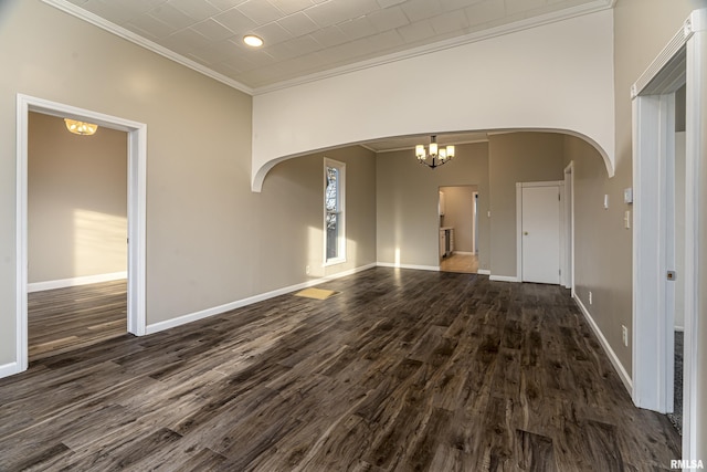 spare room featuring baseboards, arched walkways, dark wood-style flooring, crown molding, and a chandelier