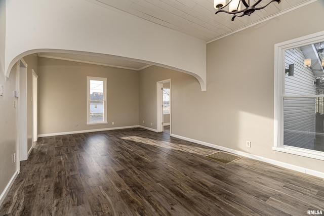 empty room featuring arched walkways, ornamental molding, dark wood-style flooring, and an inviting chandelier