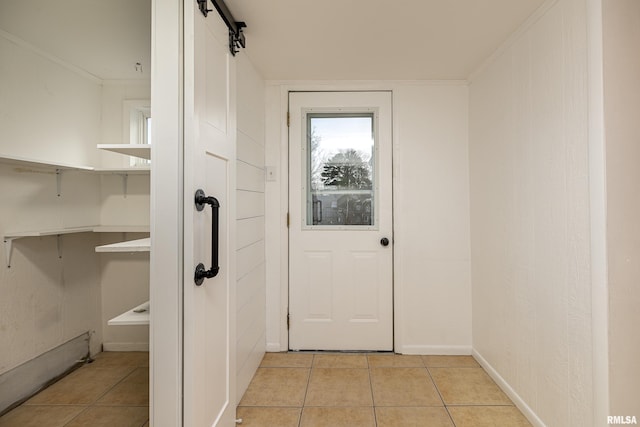 doorway featuring light tile patterned floors, crown molding, baseboards, and a barn door