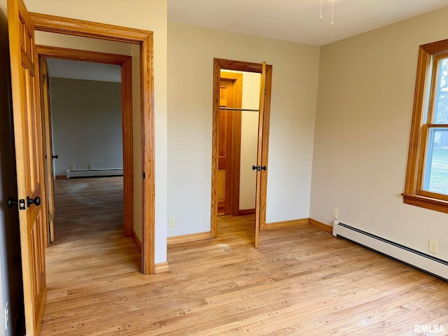 unfurnished bedroom featuring a baseboard radiator, baseboards, and light wood finished floors