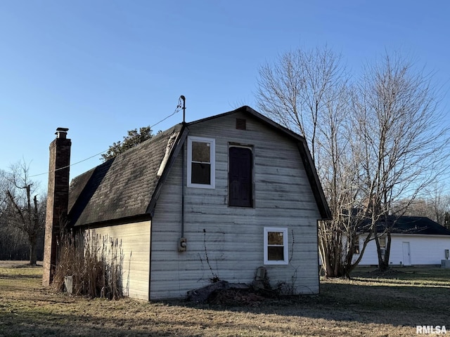 view of home's exterior featuring a barn, an outbuilding, a chimney, and a gambrel roof