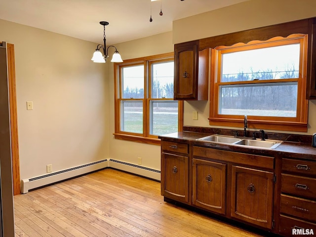 kitchen with light wood-type flooring, hanging light fixtures, dark countertops, and a sink