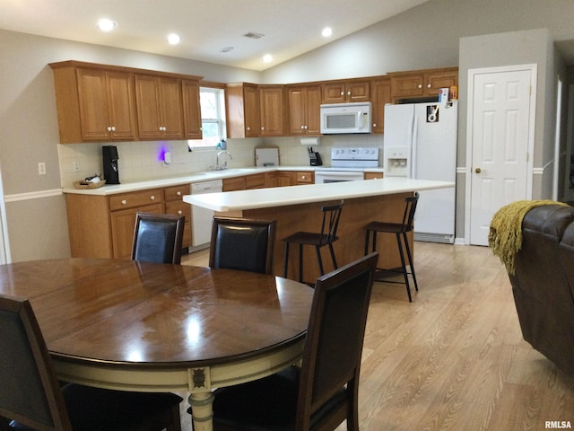 kitchen with white appliances, vaulted ceiling, light countertops, a center island, and light wood finished floors