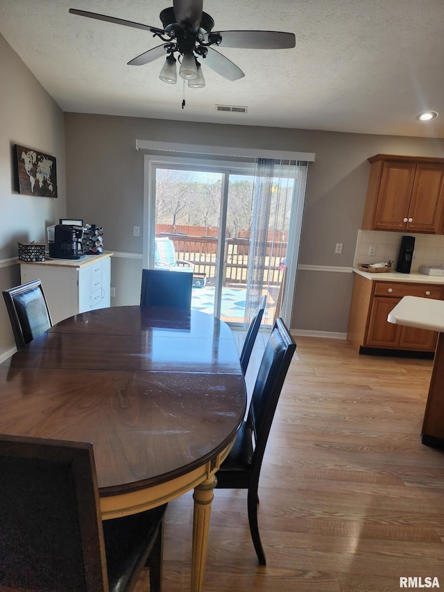 dining space with baseboards, visible vents, light wood-style flooring, and a textured ceiling