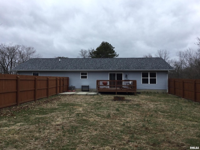 rear view of house with a shingled roof, a fenced backyard, a lawn, and a wooden deck