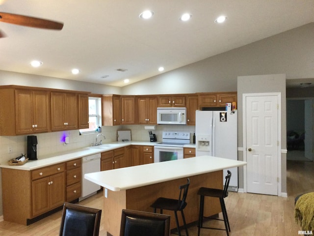 kitchen with lofted ceiling, white appliances, light wood finished floors, and a sink