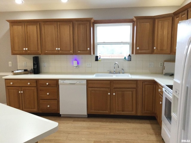 kitchen with white appliances, tasteful backsplash, brown cabinetry, light wood-type flooring, and a sink