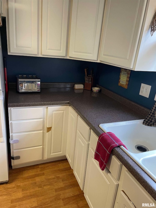 kitchen with dark countertops, light wood-style flooring, white cabinetry, and a sink